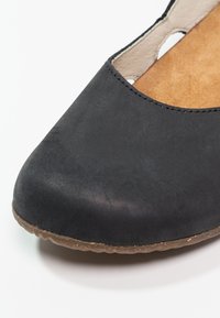 Chaussure plate en daim noir avec un bout rond, un design ajouré et une semelle intérieure texturée en tan, dotée d'une semelle en caoutchouc flexible.