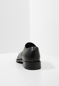 Chaussure en cuir noir à finition lisse, bout arrondi et petit talon. Présente un design simple et une silhouette élégante.