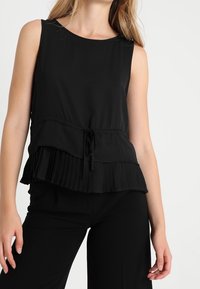 Svart ärmlös topp med en veckad nederdel och snörning vid midjan, tillverkad av lättviktigt material.