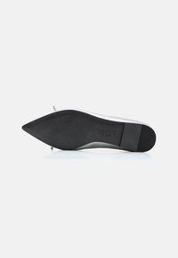 Chaussure à bout pointu avec une tige en métal argenté, semelle en caoutchouc noir et semelle intérieure texturée ; elle dispose d'un petit talon et de peu de matériel.