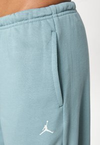 Pantaloni della tuta azzurro chiaro con una texture morbida, caratterizzati da tasche laterali e un logo Jumpman bianco vicino alla tasca sinistra.