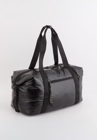 Czarna nylonowa torba sportowa o błyszczącej fakturze, podwójne czarne uchwyty, przednia kieszeń na zamek błyskawiczny z wielokolorowym uchwytem oraz okrągły kształt.