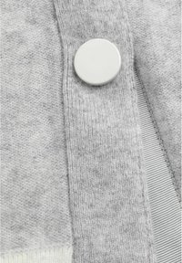 Cardigan en tricot gris avec un grand bouton blanc, texture côtelée et tissu doux présentant des variations de teinte subtiles.
