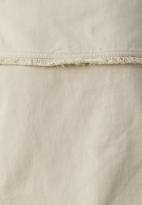 Beige bomullstoff med et synlig diagonalvevingsmønster, med råkanter og frynsete detaljer langs den øverste søm.