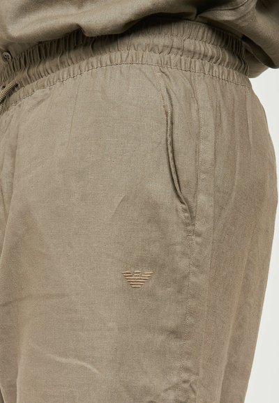 Pantaloni leggeri color khaki con vita elastica, tasche laterali e un piccolo logo ricamato di una tonalità più chiara.