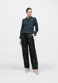 Giacca in tweed blu scuro con bottoni dorati e tasche con pattina, abbinata a pantaloni a gamba larga in pelle nera e décolleté grigio chiaro con punta a punta.