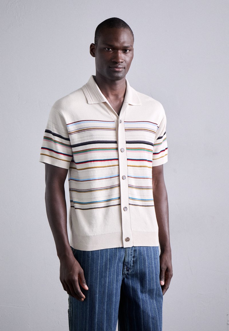 Korte mouwen crème shirt met meerkleurige horizontale strepen en een knoopsluiting aan de voorkant, gecombineerd met blauw gestreepte jeans.