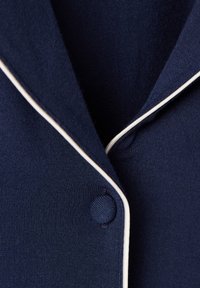 Mörkblått tyg med en slät textur, med vit piping längs med kragen och en rund knappdetalj nära slaget.