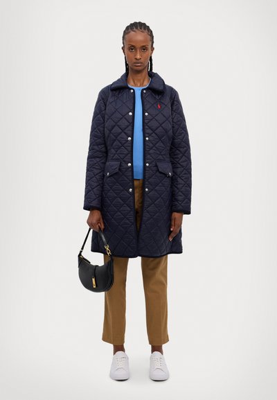 Jūras flotes šūtais mētelis ar apkakli, priekšējām kabatām un sudraba pogām, apvienots ar zilu augšu, brūnām biksēm un baltajiem sporta apaviem, turot melnu somu.