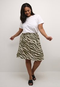 Grüner und cremefarbener Rock mit Zebra-Streifen und elastischem Bund, kombiniert mit einem schlichten weißen T-Shirt und schwarzen Sandalen mit offenem Zehenbereich.