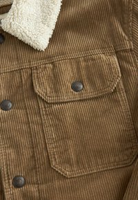 Poche de veste en velours côtelé marron avec rabat et bouton-pression métallique, dotée d'un col en sherpa crème.