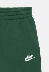 Pantalon de survêtement Nike vert foncé avec taille élastique et logo Nike blanc brodé au-dessus de la poche sur le côté droit.