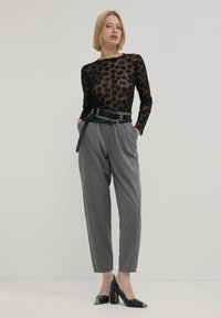 Haut en maille noire avec motif de roses, pantalon à rayures grises, ceinture noire et escarpins noirs avec accents argentés. Texture lisse et design ajusté.