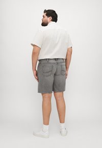 Shorts din denim gri, cu croi dreaptă și tivuri răsucite, asortați cu o cămașă albă cu dungi și mâneci scurte. Adidașii albi completează ținuta.