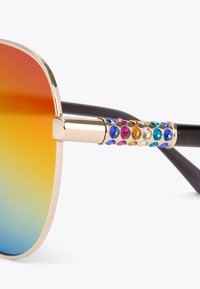 Occhiali da sole con montatura dorata e lenti sfumate che passano dall'arancione al blu. Presentano colori vivaci di strass sul lato della stanghetta.