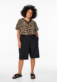 Blouse à manches courtes imprimé léopard, short noir ajusté et sandalesplates noires. La blouse présente un col en V avec une bordure en dentelle.