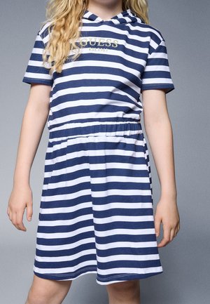 Niña con vestido de manga corta de rayas azul marino y blanco con capucha, cintura elástica y logo "GUESS est. 1981" en el pecho.