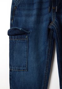Donkerblauwe denim broek met een voorzak en een zij cargozak. De stof heeft een gestructureerde weving met gele stiksels.