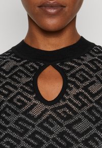 Pull noir tricoté avec un motif géométrique texturé, présentant une encolure à trou de serrure et un col noir côtelé.