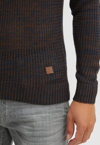 Strickpullover in Dunkelblau und Braun, mit horizontalem Rippenmuster. Enthält ein kleines Logo-Emblem aus Leder an der unteren Seite.