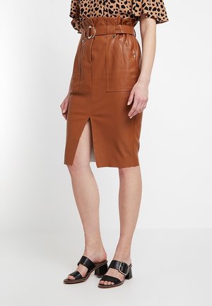 Vrouw draagt een bruine leren rok met riem en voorsplit, gecombineerd met een top met luipaardprint en zwarte open-toe hakken met gespen.
