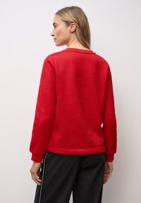 Rote Sweatshirt mit schlichter Gestaltung, Rundhalsausschnitt, langen Ärmeln und gerippten Bündchen; kombiniert mit grauen Jogginghosen mit seitlichen Streifen.