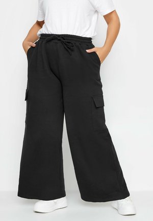 Pantalons cargo larges noirs avec une taille élastique et un cordon de serrage ajustable, des poches latérales, et un tissu lisse et texturé.