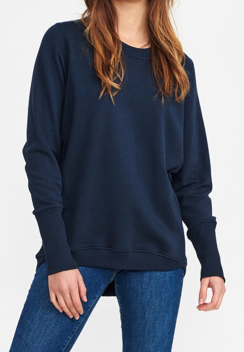 Sudadera azul marino de un material suave y elástico con cuello redondo y puños acanalados, que presenta un ajuste relajado y aberturas laterales.