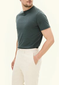 Mörkgrön t-shirt med kort ärm i mjukt tyg, tillsammans med ljusbeiga byxor med rak passform och sidofickor.