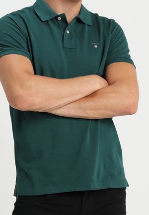 Ciemnozielona koszulka polo z kołnierzykiem, krótkimi rękawami i logo GANT na klatce piersiowej. Wykonana z miękkiej bawełny, o gładkiej fakturze i bez wzorów.
