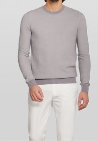 Suéter gris claro de punto con puños y dobladillo acanalados, que presenta un patrón texturizado. Usado con pantalones blancos para contraste.