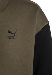 Felpa Puma con blocchi di colore verde oliva e nero, tessuto testurizzato, maniche corte e logo ricamato sul petto.