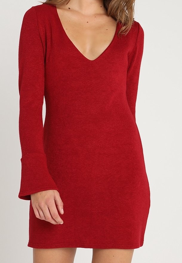 Röd stickad klänning med långa klockärmar och djup V-ringning. Tyget verkar mjukt och texturerat, vilket ger en figurnära siluett.