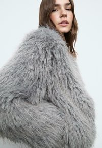 Chlpatá šedá bunda s jemnou, textúrovanou tkaninou, voľným strihom a širokými rukávmi. Dizajn kladie dôraz na teplo a pohodlie.