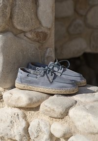 Grå ruskindsespadriller med vævede jutesåler, to huller og matchende snørebånd, placeret på en stens overflade.