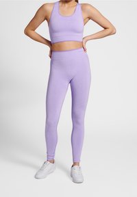 Světlý fialový sportovní set skládající se z těsného crop topu a legín s vysokým pasem, vyrobený z elastického materiálu, doplněný bílými teniskami.