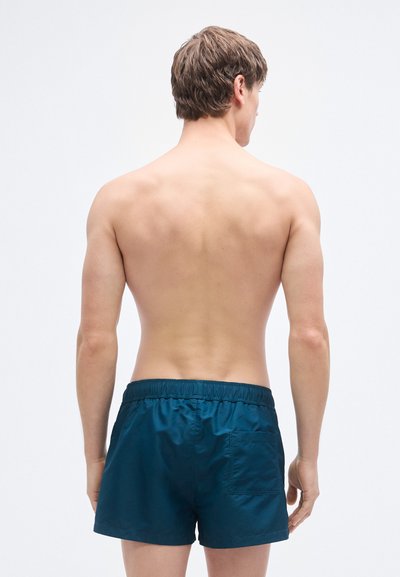Ανδρικά μαγιό σορτς σε βαθύ τιρκουάζ, με μαλακή, απαλή υφή, ελαστική μέση και μία τσέπη στο πίσω μέρος. Απλός σχεδιασμός, μήκος μέχρι το μέσο μηρού.