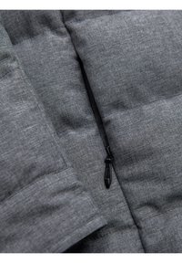 Gros plan d'une veste matelassée gris foncé avec une fermeture éclair noire partiellement fermée et des coutures détaillées.