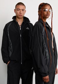 Vestes noires zippées en matériau léger, avec des accents argentés, des poignets élastiques et un motif discret sur les côtés.