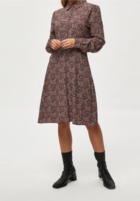 Robe à manches longues avec un motif floral rouge et noir, dotée d'un col et d'une taille élastique. Portée avec des bottines noires. Tissu lisse.