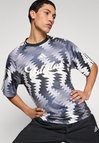 Αθλητικό t-shirt με κοντά μανίκια σε αποχρώσεις του γκρι με ζιγκ-ζαγκ μοτίβο, με λευκό λογότυπο και μαύρες λεπτομέρειες, κατασκευασμένο από λείο ύφασμα.