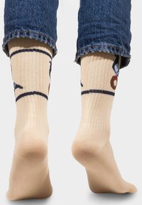 Skarpetki w kolorze beżowym do kolan z żebrowanym wzorem, z niebieskimi akcentami i zabawnym motywem pączka, zestawione z podwiniętymi dżinsami.