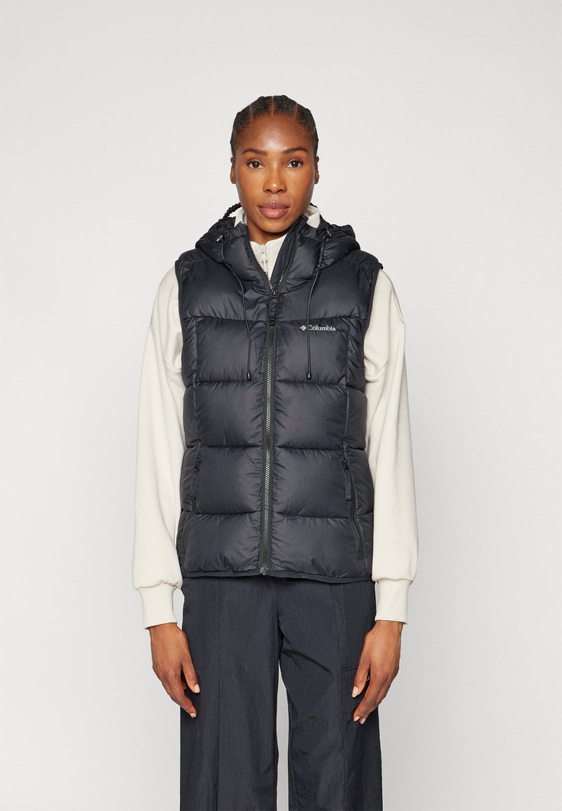 Czarna pufowa kamizelka z kapturem, z przodu zapinana na zamek błyskawiczny, z dwiema bocznymi kieszeniami oraz pikowanym wzorem. Noszona na jasnym topie.