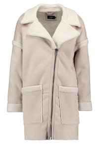 Abrigo color crema con cuello y puños de borrego, que presenta dos bolsillos frontales y una cremallera de longitud completa. Textura suave y diseño de gran tamaño.