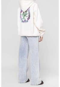 Bílá oversize mikina s grafickým designem na zádech, doplněná o světle modré široké džíny s vybledlým vzhledem.