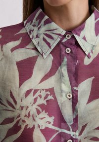 Floral button-up shirt featuring a purple and pale green design, made of lightweight fabric with a pointed collar and subtle sheen.