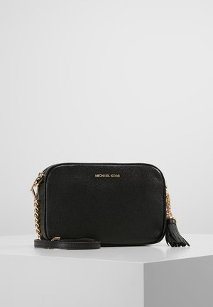 Czarna torba Michael Kors na ramię z złotym łańcuszkiem, detalem z frędzlem i fakturowaną powierzchnią skóry na białym piedestale i jednolitym tle.