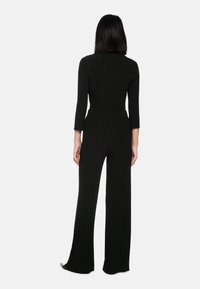 Black ribbed jumpsuit with long sleeves and wide legs. Features a fitted waist and textured fabric. Back view shows seamless design.