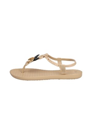 Sandalia plana beige con tira en T y tira en el tobillo, con detalles decorativos en negro y dorado en la tira superior.