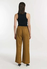 Zwarte tanktop gecombineerd met wijde, hoog-waisted mosterdkleurige broek van textuurstof met een elastische tailleband.